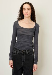 Långärmad, mörkgrå topp med rundad halsringning och rynkad textur. Matchad med högmidjade svarta jeans med framlommor.