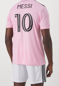 Vaaleanpunainen jalkapallojersey, jossa on mustat yksityiskohdat; takana lukee "MESSI" ja numero "10". Päällä valkoiset shortsit, joissa on mustat raidat.