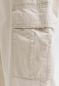 Poche cargo beige en tissu avec rabat et coutures apparentes sur un pantalon ou un short.