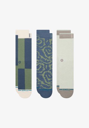 Tres pares de calcetines: el de la izquierda tiene patrones geométricos en azul marino y verde; el del centro presenta un diseño abstracto en azul y verde; el de la derecha es de color verde claro con acentos en beige.