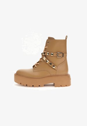 Tanfarbene Lederstiefeletten mit einer massiven Sohle, ausgestattet mit Schnürsenkeln, einem Riemen mit Schnalle und goldenen Nieten als dekorative Akzente.