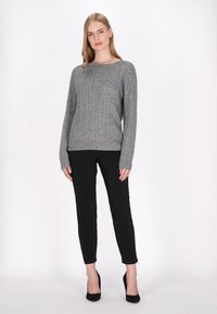Szürke, kötött pulóver kerek nyakkivágással és bordás mandzsettával, fekete, slim-fit nadrággal és fekete magas sarkú cipővel párosítva.
