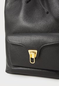 Zaino in pelle nera con superficie testurizzata, dotato di una chiusura dorata e una tasca frontale. La chiusura a coulisse sulla parte superiore permette un facile accesso.