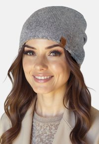 Grå strikket hue med et struktureret mønster og en brun læderlogoetiket, båret komfortabelt, med en blød, afslappet pasform.