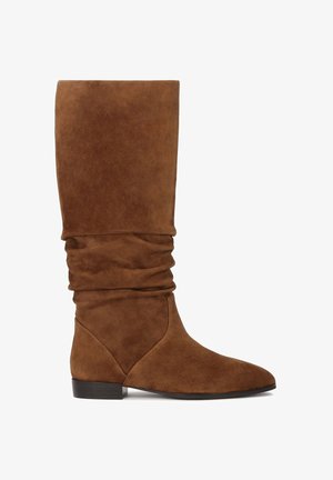 Botă maro din suede, până la genunchi, cu un design relaxat, vârf ascuțit și toc mic blocat. Prezintă o textură netedă și o siluetă simplă.