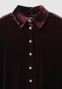 Camicia in velluto borgogna con colletto classico, caratterizzata da cinque bottoni in gioiello ben evidenti lungo il davanti per un tocco di dettaglio e texture.
