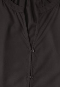 Gros plan de l'avant d'une chemise en tissu noir montrant le col et deux boutons foncés sur une patte verticale.