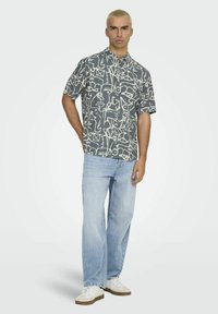 Kortærmet skjorte i mørkegrå med hvide abstrakte mønstre, knaplukning. Parret med lyseblå jeans og hvide sneakers.