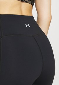 Närbild av en person som bär svarta högmidjade Under Armour leggings och en mönstrad sport-bh, som visar baksidan och midjeområdet.