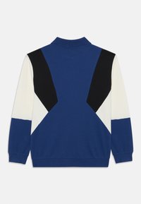 Blå og svart fargeblokkert sweatshirt med polo-krage, med geometriske mønstre og ribbestrikkede mansjetter. Myk strikket stoff.