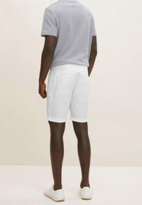 Pantaloni corti bianchi con orli ripiegati, abbinati a una maglietta grigia a maniche corte. Le gambe del modello sono visibili e indossa sneakers bianche.