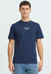 Laivastonsininen puuvillainen pyöreäkauluksinen t-paita, jossa on lyhyet hihat ja valkoinen "UNLIMITED"-kuvio rinnassa.