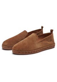 Chaussures en daim à enfiler d'une couleur marron chaud, dotées d'une semelle en jute tressé et d'un design minimaliste avec des panneaux élastiques sur les côtés pour un enfilage facile.