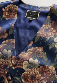 Bluse aus navyblauem Satin mit floralem Muster und gestickten großen orange- und cremefarbenen Blumen. Mit tiefem V-Ausschnitt und dekorativen Knöpfen.