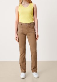 Żółta prążkowana bluzka na ramiączkach i jasno brązowe dopasowane spodnie z tylnymi kieszeniami, z przodu z zapięciem na guziki i zamek błyskawiczny, w połączeniu z białymi trampkami.