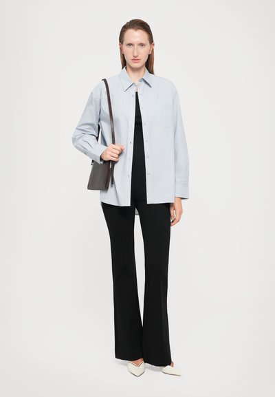 Light blue button-up shirt, black top, black flared pants, and white pointed-toe shoes. Model holds a small gray bag.
