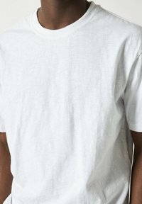 Vit kortärmad t-shirt i lättviktigt bomull. Texturerat tyg med rundad halsringning, något lös passform, och minimala design detaljer.