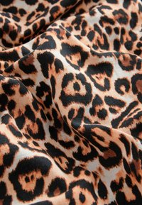 Tissu imprimé léopard présentant de grandes taches noires et orange sur un fond beige clair ; texture lisse avec un léger éclat.