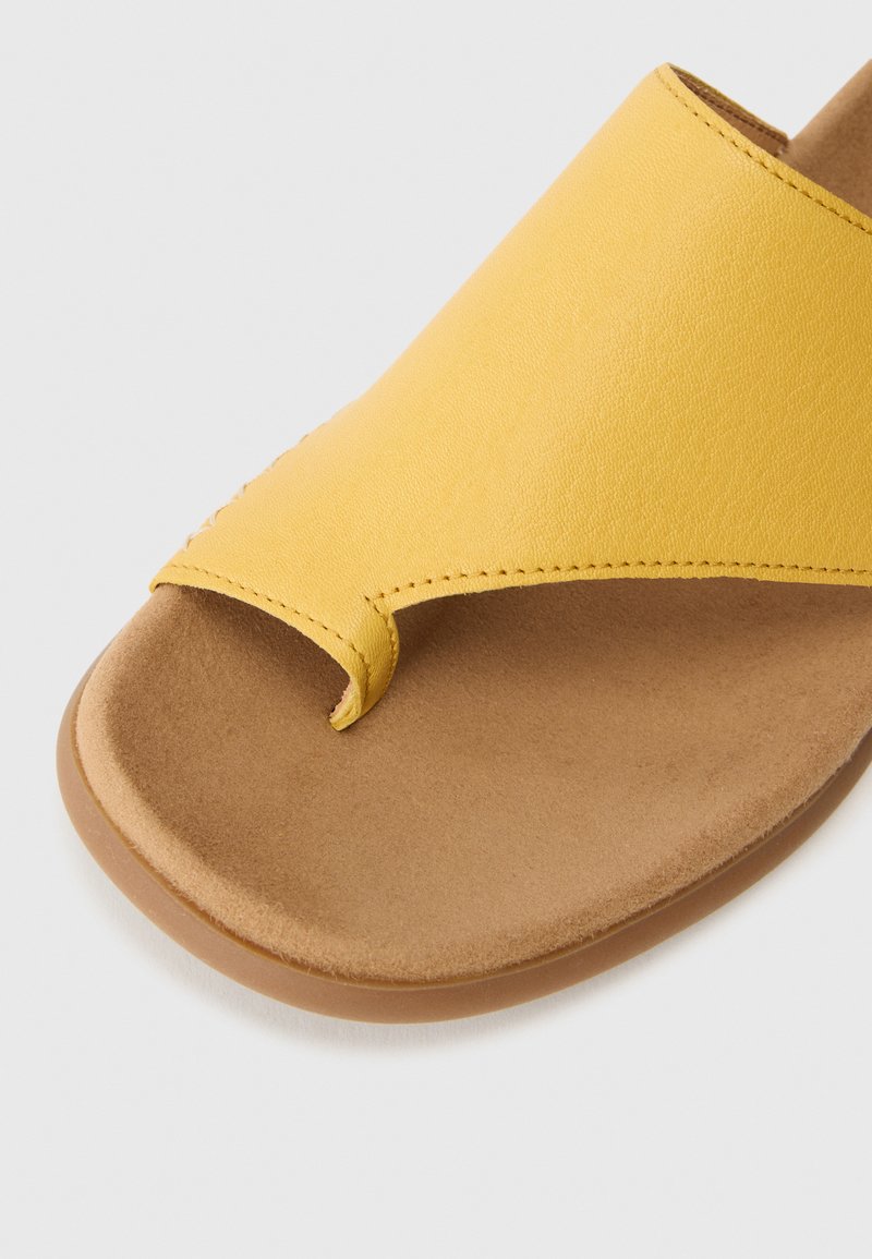 Sandale à glissement en cuir jaune avec une boucle pour les orteils, surface lisse et semelle intérieure contrastante couleur tan. Semelle plate avec des caractéristiques de design minimalistes.