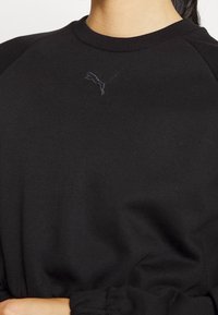 Černá mikina s kulatým výstřihem a raglánovými rukávy. Má na hrudi vyšité logo Puma tmavým vláknem. Jemná textura.