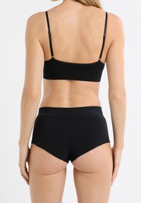 Bralette nero con spalline sottili e design texturizzato, abbinato a pantaloncini coordinati a vita alta, caratterizzati da una finitura liscia.