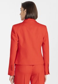 Czerwona, dopasowana marynarka o strukturalnym kroju, gładkiej fakturze i jednorzędowym zapięciu. Na rękawach cztery ozdobne guziki.