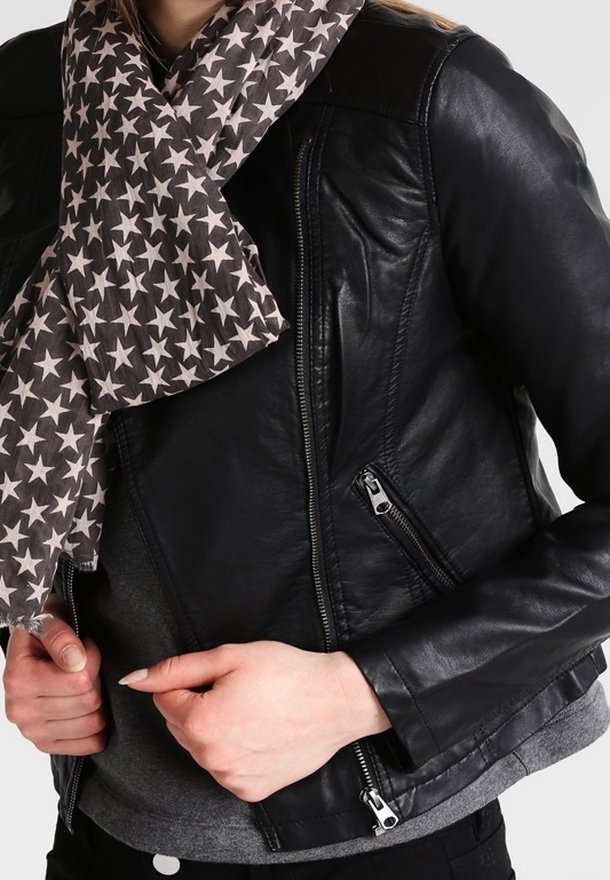 Personne portant une veste en cuir noire et une écharpe grise avec des étoiles blanches, ajustant la fermeture éclair de la veste avec les deux mains.