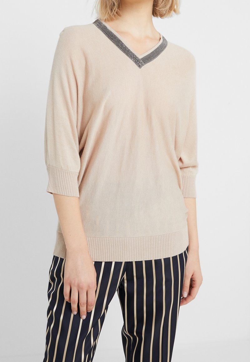 Pull en tricot beige avec un col en V et un détail contrastant au niveau du col noir. Il présente des manches trois-quarts et un ourlet côtelé.