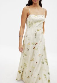 Maxi šaty z ľahkej, textúrovanej látky v krémovej farbe, so vzorom kvetov s zelenými a oranžovými akcentmi. Tenké ramienka a štvorcový výstrih.
