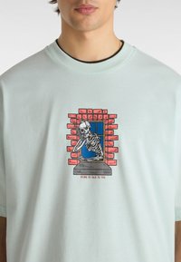 T-shirt in cotone verde chiaro con grafica di uno scheletro alla finestra, circondato da mattoni rossi, con il testo "MORIRE WANTING DI PARLARE CON TE".