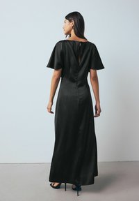 Fekete, bokáig érő ruha sima selyemszerű felülettel, rövid, fodros ujjakkal és kulcslyuk hátkivágással. Magassarkú cipővel párosítva.