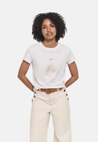 T-shirt blanc à manches courtes avec une illustration en feuille d'or sur le devant, associé à un pantalon beige clair à jambes larges et une ceinture marron.