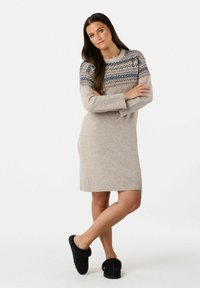 Beige sweaterkjole med mønstret yoke i blå og pink. Blød strikket tekstur, ribbede manchetter og kant. Sorte hjemmesko med pelsfor fuldender looket.