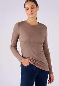 Maglietta a maniche lunghe marrone a costine con scollatura rotonda, design aderente e texture liscia abbinata a jeans in denim blu scuro.