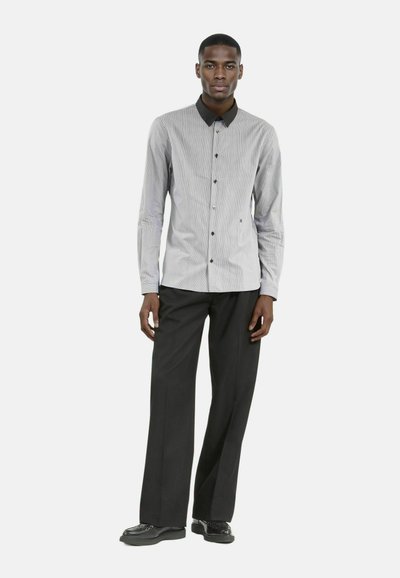 Camisa de botones a rayas en blanco y gris con cuello negro, combinada con pantalones anchos negros y zapatos negros. Textura de tela suave.