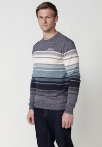 Gebreide ronde hals trui met horizontale strepen in tinten blauw, crème en marineblauw. Voorzien van een ribgebreide manchet en zoom.