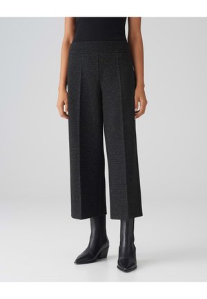 Zwarte, cropped wijd-uitlopende broek met verticale textuur en plooien; gecombineerd met zwarte, puntige enkellaarsjes. Eenvoudig ontwerp van de tailleband.