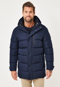 Marineblaue Steppjacke mit horizontalen Nähten, vorderen Knöpfen, Reißverschlüssen und Kapuze. Verfügt über eine glatte, matte Textur und praktische Taschen.
