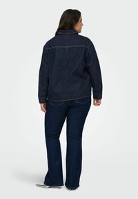 Dark denim jacket with a collared neckline, featuring a speckled pattern. Paired with dark flared jeans, viewed from the back.