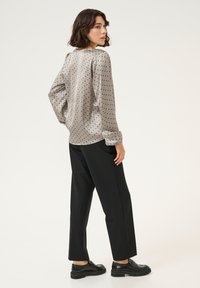 Light gray, polka-dotted blouse with long sleeves and a relaxed fit, paired with black wide-leg trousers and black shoes.