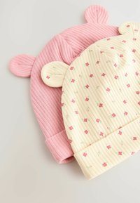 Deux chapeaux d'enfant : l'un rose à côtes avec des oreilles rondes, l'autre jaune pâle avec des motifs floraux et des côtes, tous deux avec des bords repliés.