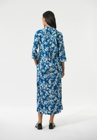 Blaues maxikleid mit floralem Muster und Dreiviertelärmeln, das eine lockere Passform, ein Rückenknotendetail und einen leichten Stoff mit glatter Textur aufweist.