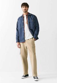 Tumesinine denimpusa punase ruudulise särkide, valge T-särgi, beežide cargo-pükste ja mustade valgete aktsentidega tossudega. Nööbid pusa taskutel.