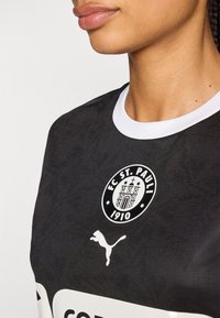 Zwart sportshirt met het FC St. Pauli-logo en witte accenten, met een ronde witte kraag en een subtiel textuurpatroon op de stof.