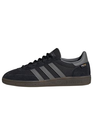 Czarny niskoprofilowy sneaker marki Adidas z szarymi paskami, zamszową i siateczkową cholewką, brązową teksturowaną podeszwą oraz metką z tkaniny CoroQuilt na pięcie.