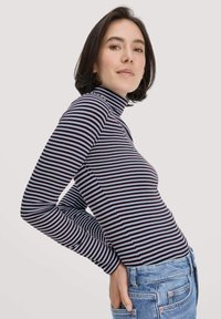 Gestreiftes langärmliges Rollkragenoberteil in Marineblau und Hellblau, figurbetonter Schnitt, glatte Textur, kombiniert mit blauen Jeans, Seitenansicht.