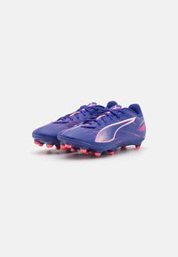 Lilla fotballsko laget av syntetisk materiale, med rosa detaljer, teksturert overflate og spisse knotter i sålen for bedre grep.