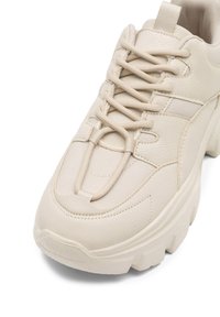 Beżowe sneakersy z teksturowaną skórzaną cholewką, wyściełanym językiem, elastycznymi sznurówkami i grubą gumową podeszwą. Charakteryzują się smukłym designem z minimalnymi akcentami.