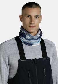 Gaiter de cuello multicolor en tela suave y elástica con patrones abstractos en azul y blanco, usado sobre una camiseta de manga larga gris y un overol negro.