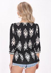 Blusa nera con motivo floreale e geometrico bianco, maniche a tre quarti e dettagli a righe sui polsini. Tessuto dalla texture liscia.